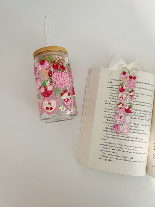 Decorative glass tumbler with floral design next to an open book on a white surface